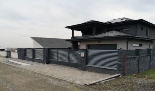 Großes, modernes Einfahrtstor aus horizontalen Aluminiumlatten, das eine Einfahrt zu einem luxuriösen Wohnhaus umgibt.