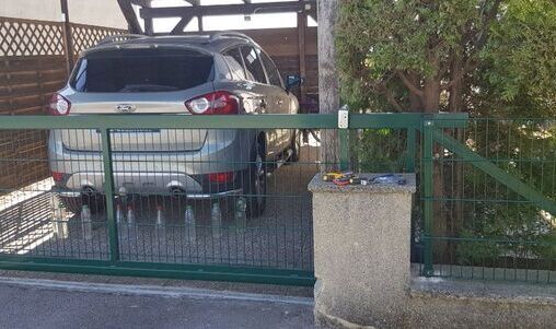 Offener Carport mit grünem Metalltor, geeignet für ein Fahrzeug.