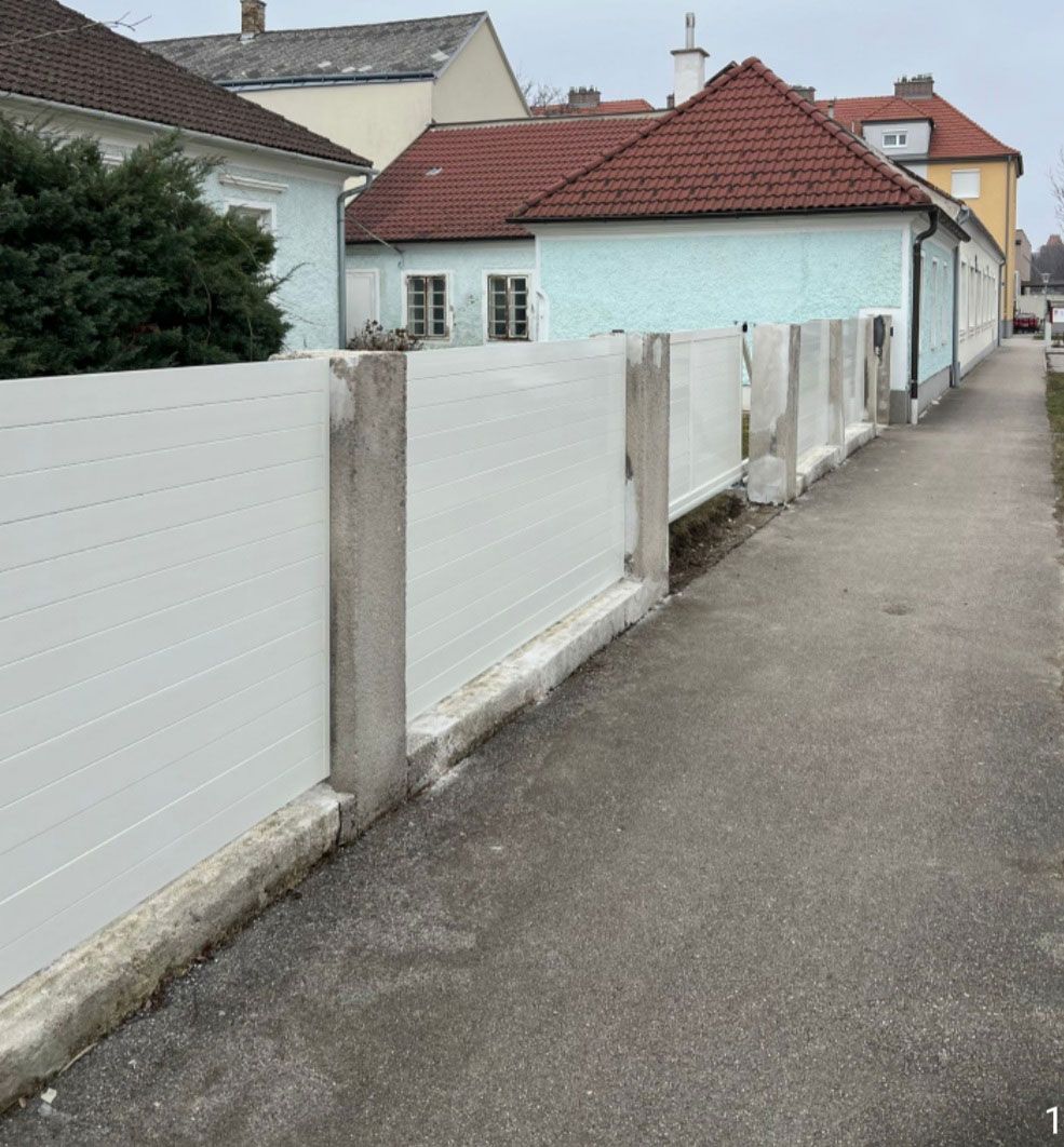 Weißer Betonzaun mit vertikalen Pfosten, der entlang eines Gehweges installiert ist.