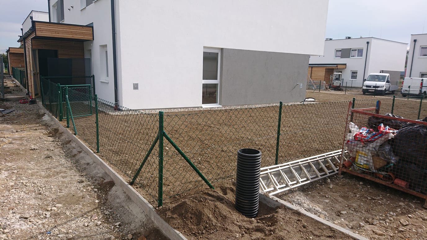Metallgitterzaun mit grünem Rahmen, der eine Wohnfläche abgrenzt, mit einer einfachen Konstruktion.