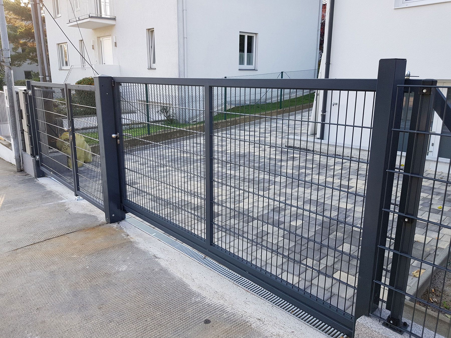 Metallgitterzaun mit rechteckigen Rahmen, mit einer Doppeltür zur Einfahrt eines Grundstücks.